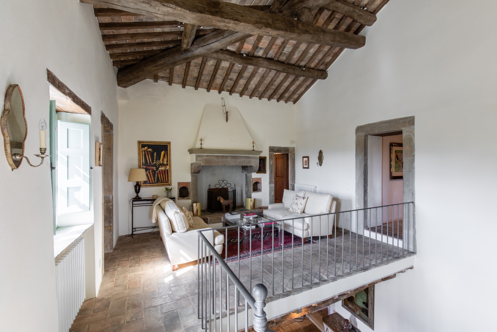 Upstairs galleried sitting room with sofas, coffee table, rug, fireplace and painting at Tenuta Cantata in Tuscany, Italy