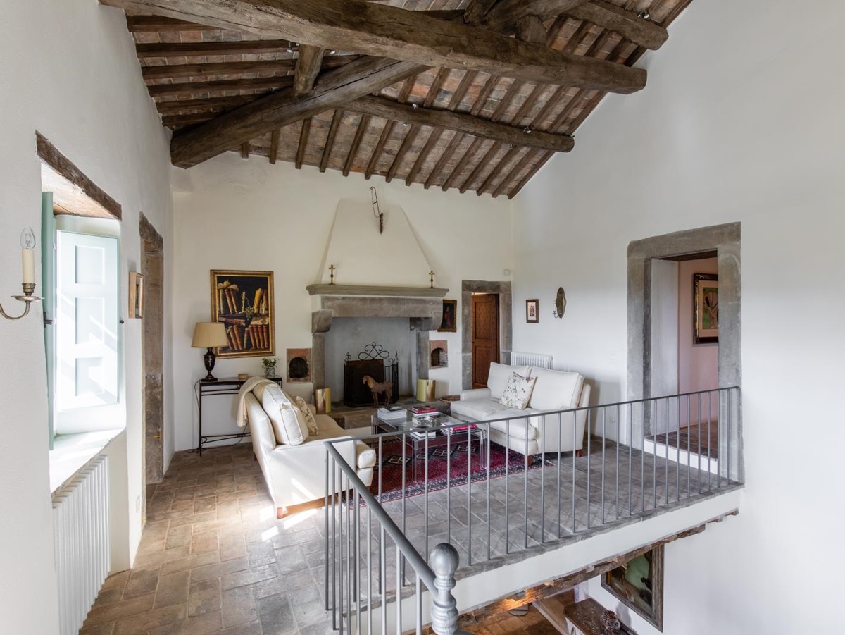 Upstairs galleried sitting room with sofas, coffee table, rug, fireplace and painting at Tenuta Cantata in Tuscany, Italy