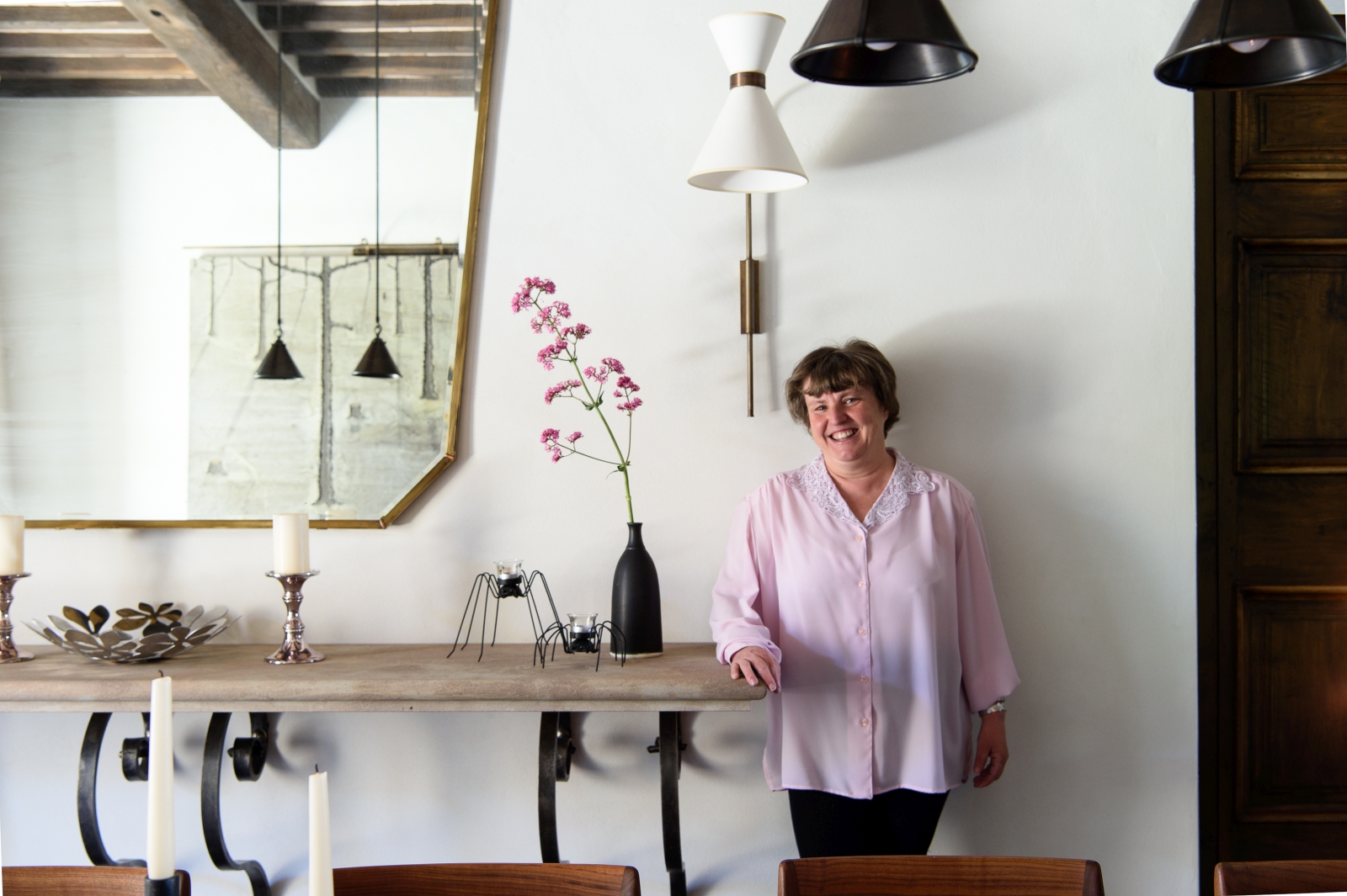 Villa manager in dining room with console table, mirror, candles, flowers and hanging lights at Tramonti in Tuscany, Italy