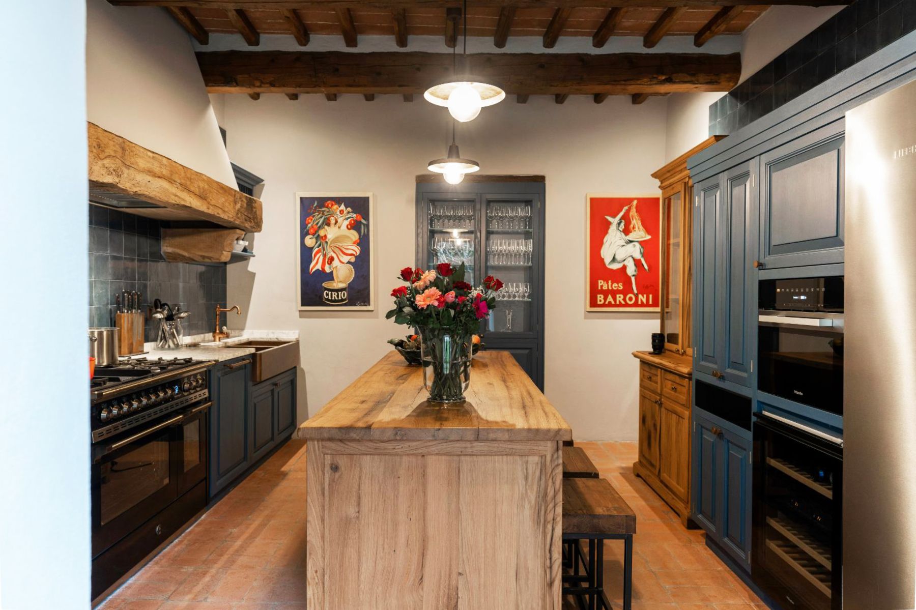 Kitchen with view of the wooden island and wooden beam with framed art at Villa Ardore in Tuscany