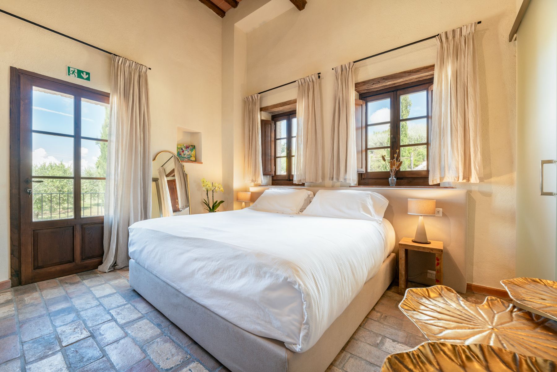 Bedroom with large double bed and windows behind the bed at Villa Cispiano in Tuscany