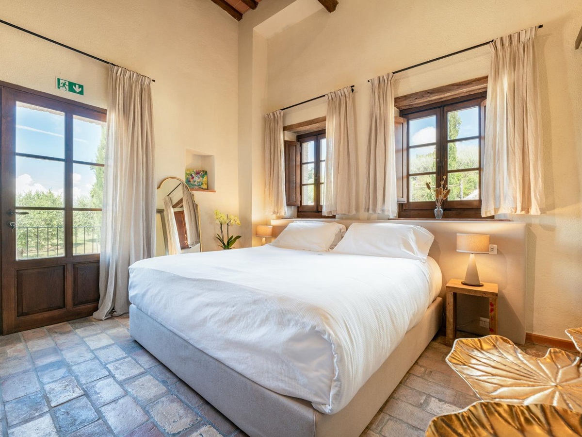 Bedroom with large double bed and windows behind the bed at Villa Cispiano in Tuscany
