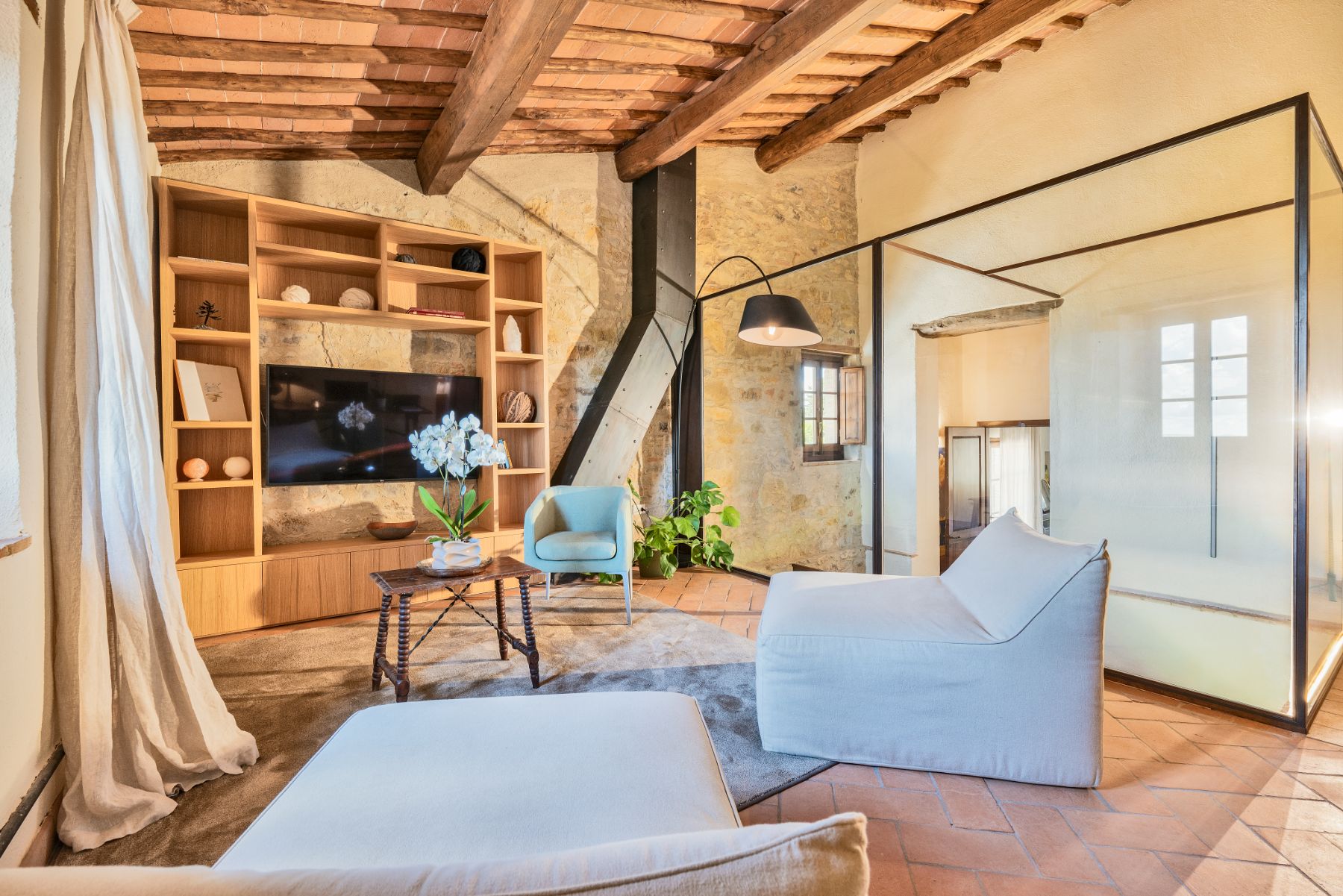 Indoor living area with large wooden shelves and comfy seats with Tv on wall at Villa Cispiano in Tuscany