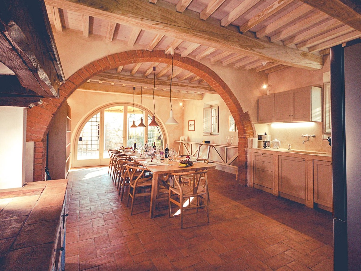 Kitchen with long dining table, hanging lights, stone archway and cupboards at Villa dell’Angelo in Tuscany, Italy
