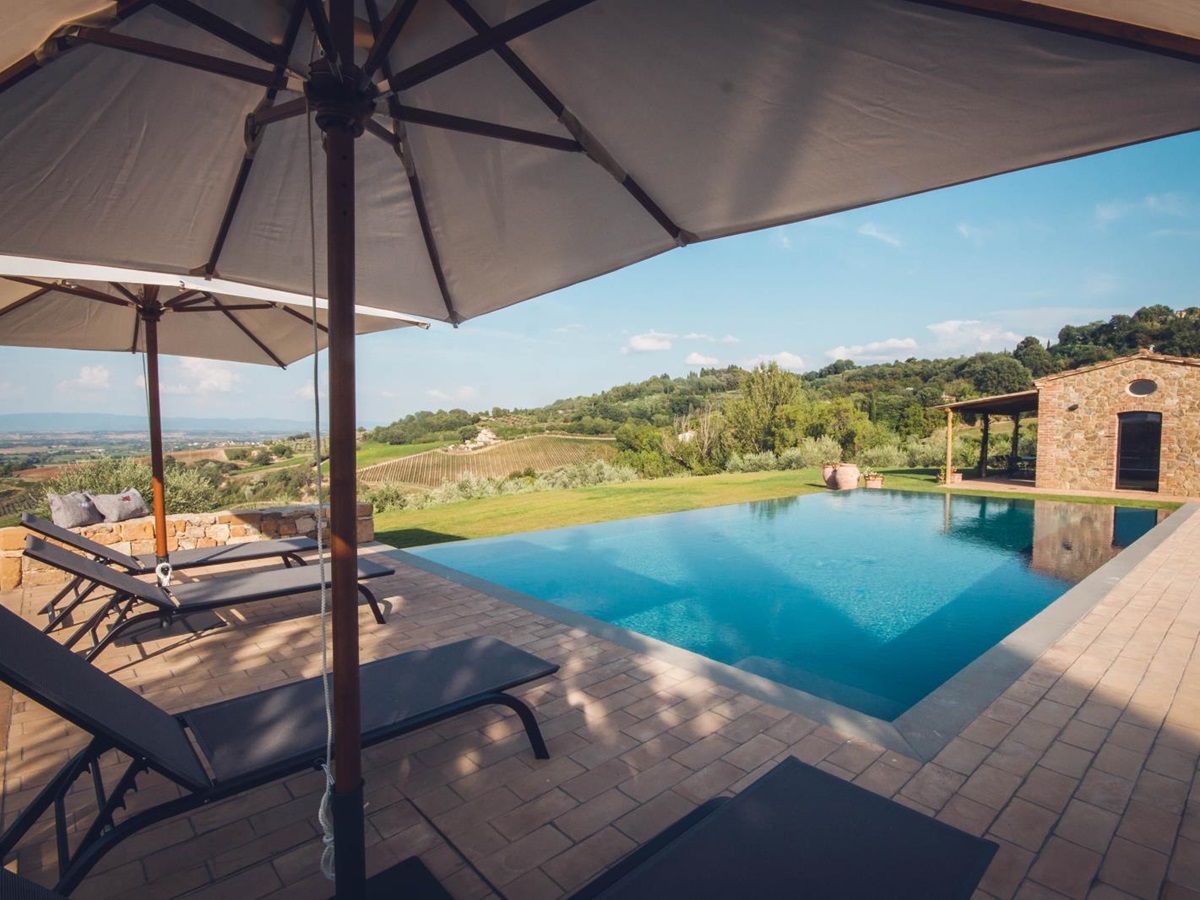 Pool and pool area with sun loungers, umbrellas, outhouse and countryside view at Villa dell’Angelo in Tuscany, Italy