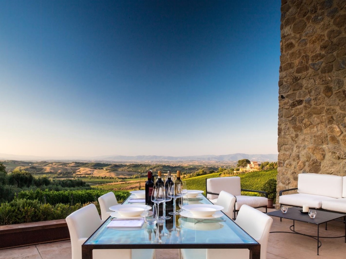 Terrace with dining table, wine, coffee table, sofas and countryside view at Villa dell’Angelo in Tuscany, Italy