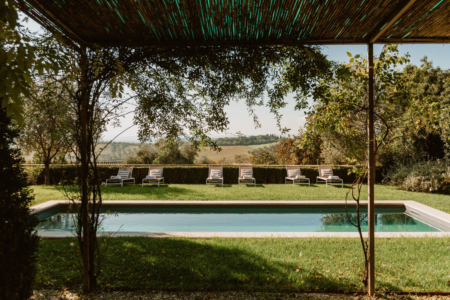 Outdoor pool area at Villa delle Vigne in Tuscany surrounded by grass with sunloungers