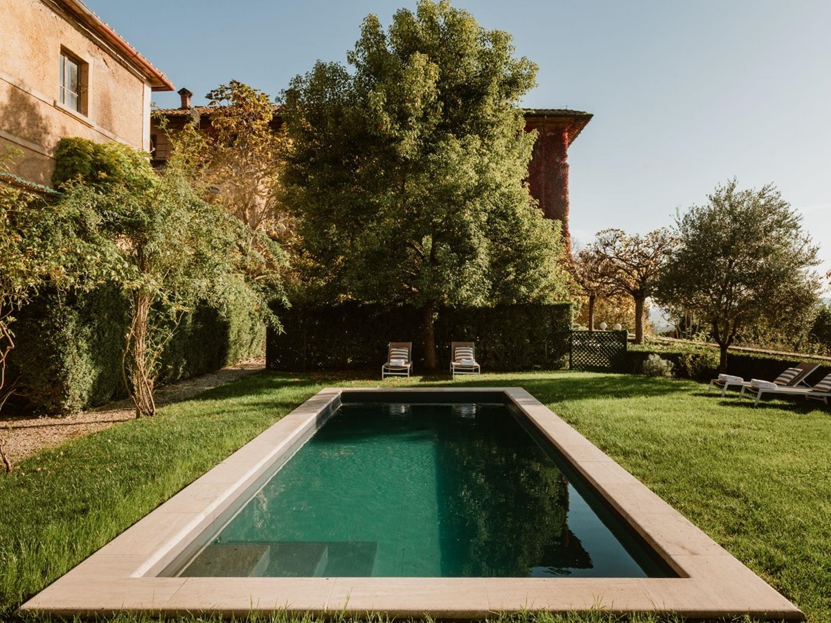 Outdoor pool area surrounded by grass and trees at Villa delle Vigne in Tuscany
