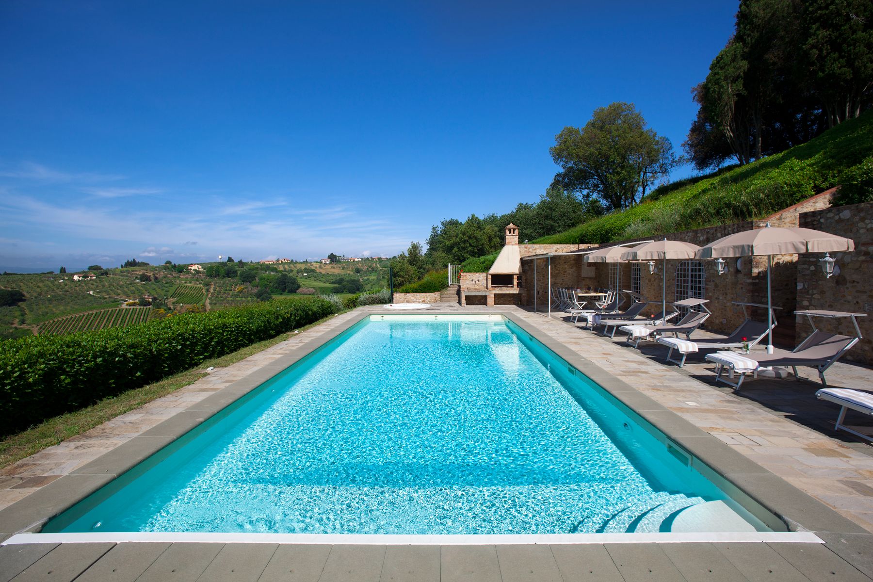 Pool area with sunbeds at the right and view of the hills on the left at Villa di Tignano in Tuscany