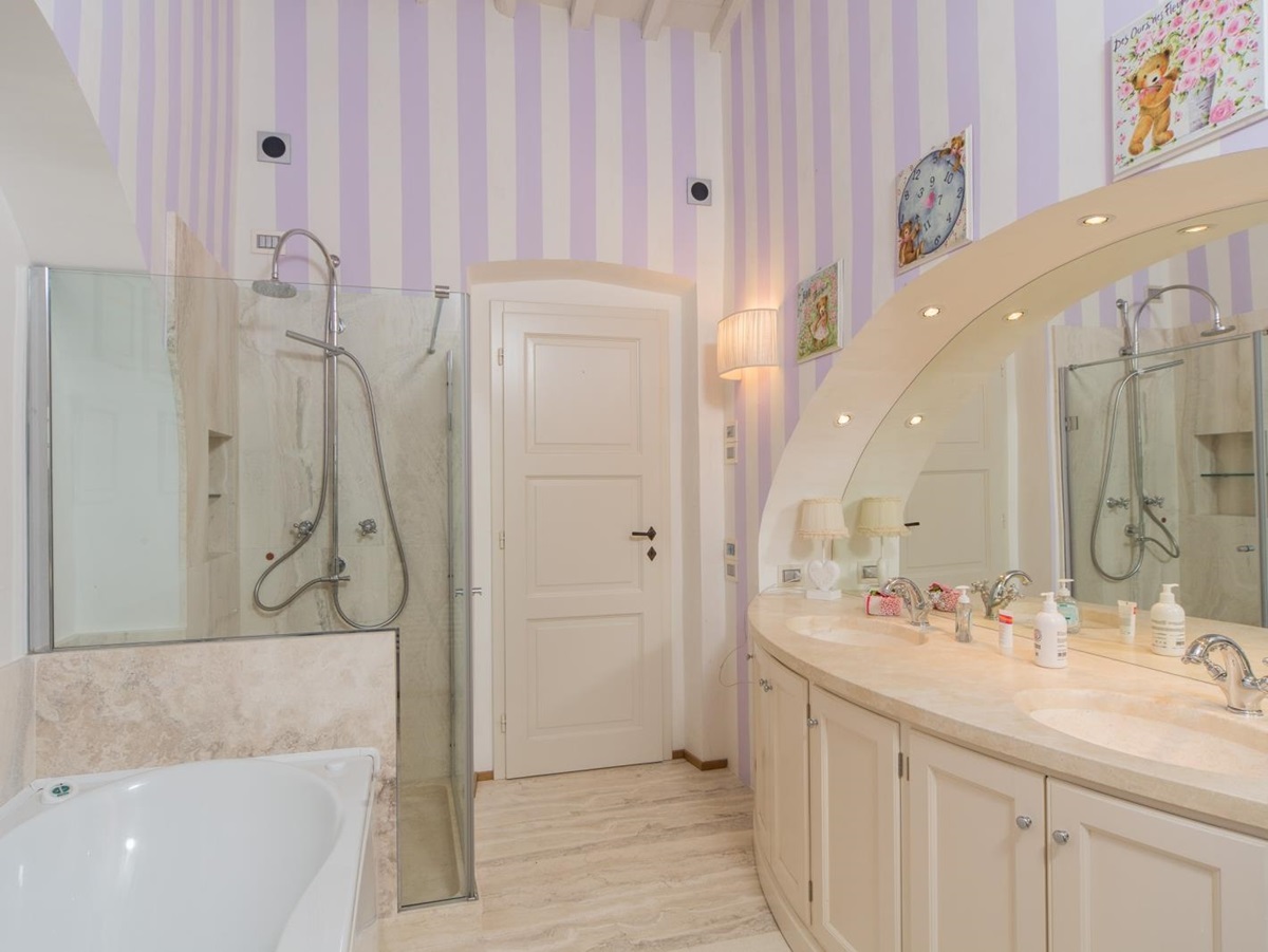 Bathroom with candy stripe walls, bath, shower, double sink and large mirror at Villa di Tignano in Tuscany, Italy