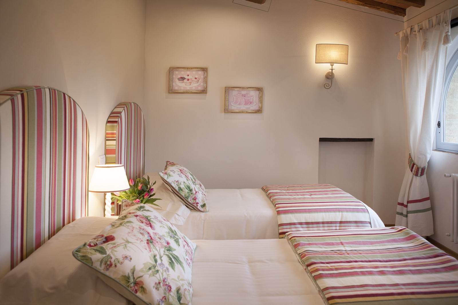 Twin bedroom with lamps, picture frames and window at Villa di Tignano in Tuscany, Italy