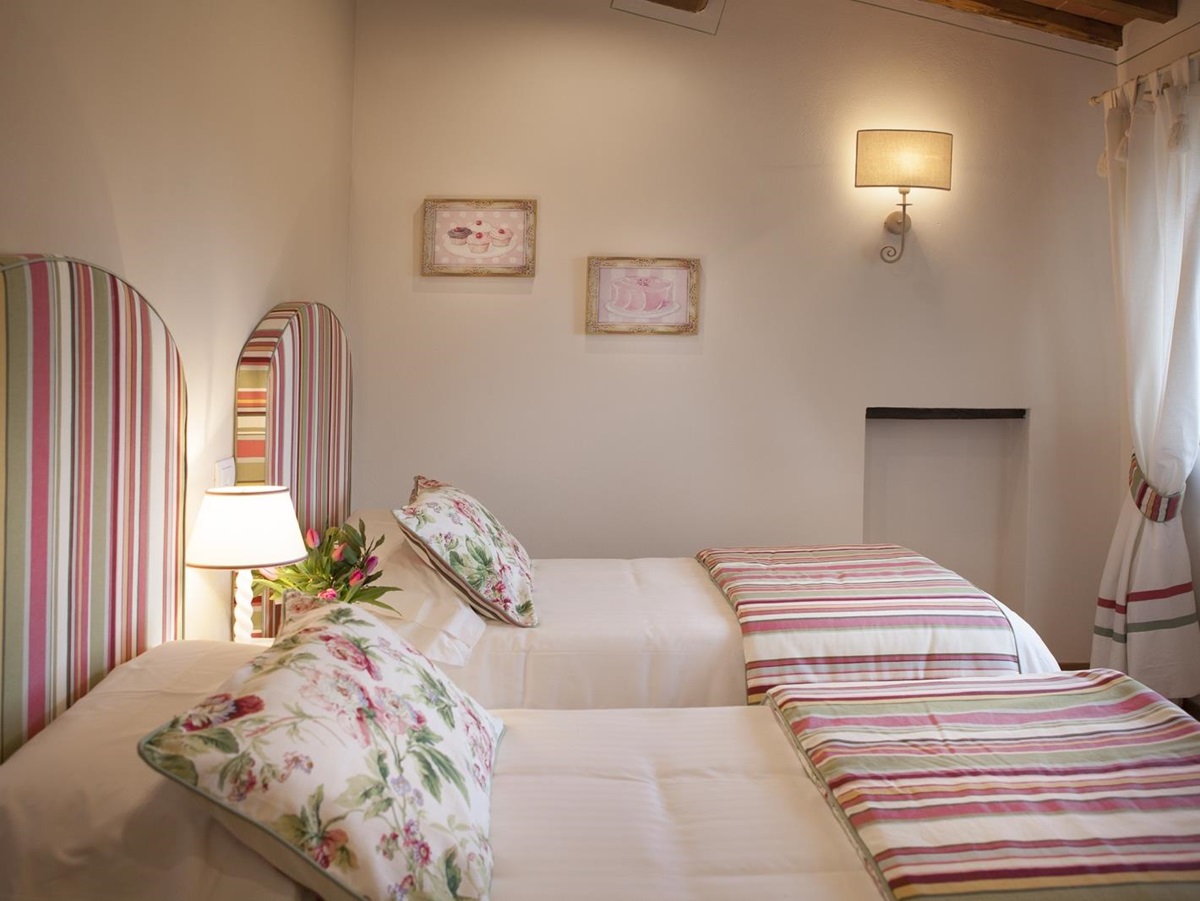 Twin bedroom with lamps, picture frames and window at Villa di Tignano in Tuscany, Italy