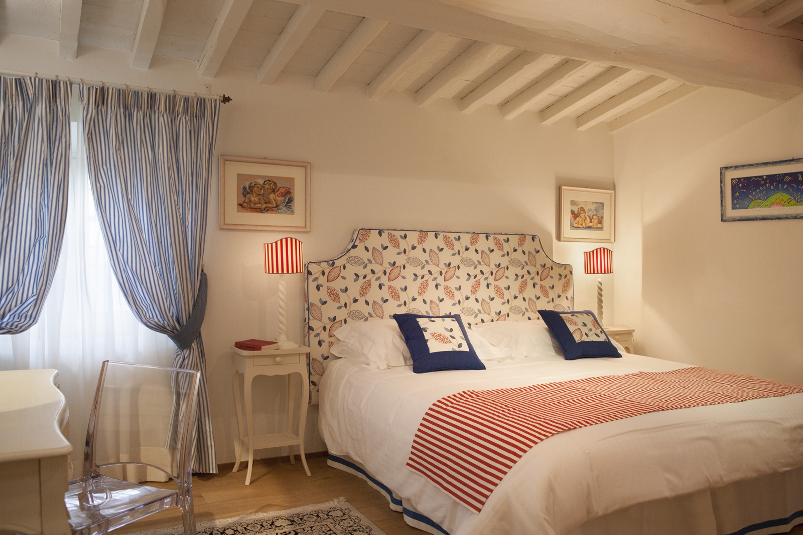 Bedroom with double bed, bedside table, blue striped curtains, lamp, desk and chair at Villa di Tignano in Tuscany, Italy