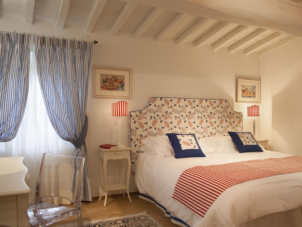 Bedroom with double bed, bedside table, blue striped curtains, lamp, desk and chair at Villa di Tignano in Tuscany, Italy