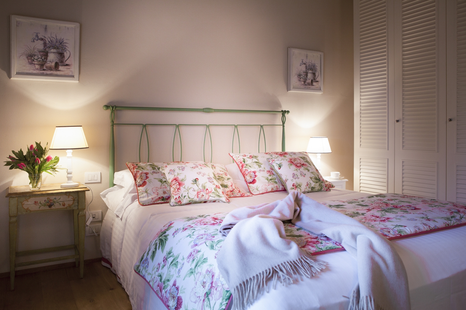 Bedroom with double bed, bedside tables, lamps, flowers, wardrobe and pictures at Villa di Tignano in Tuscany, Italy