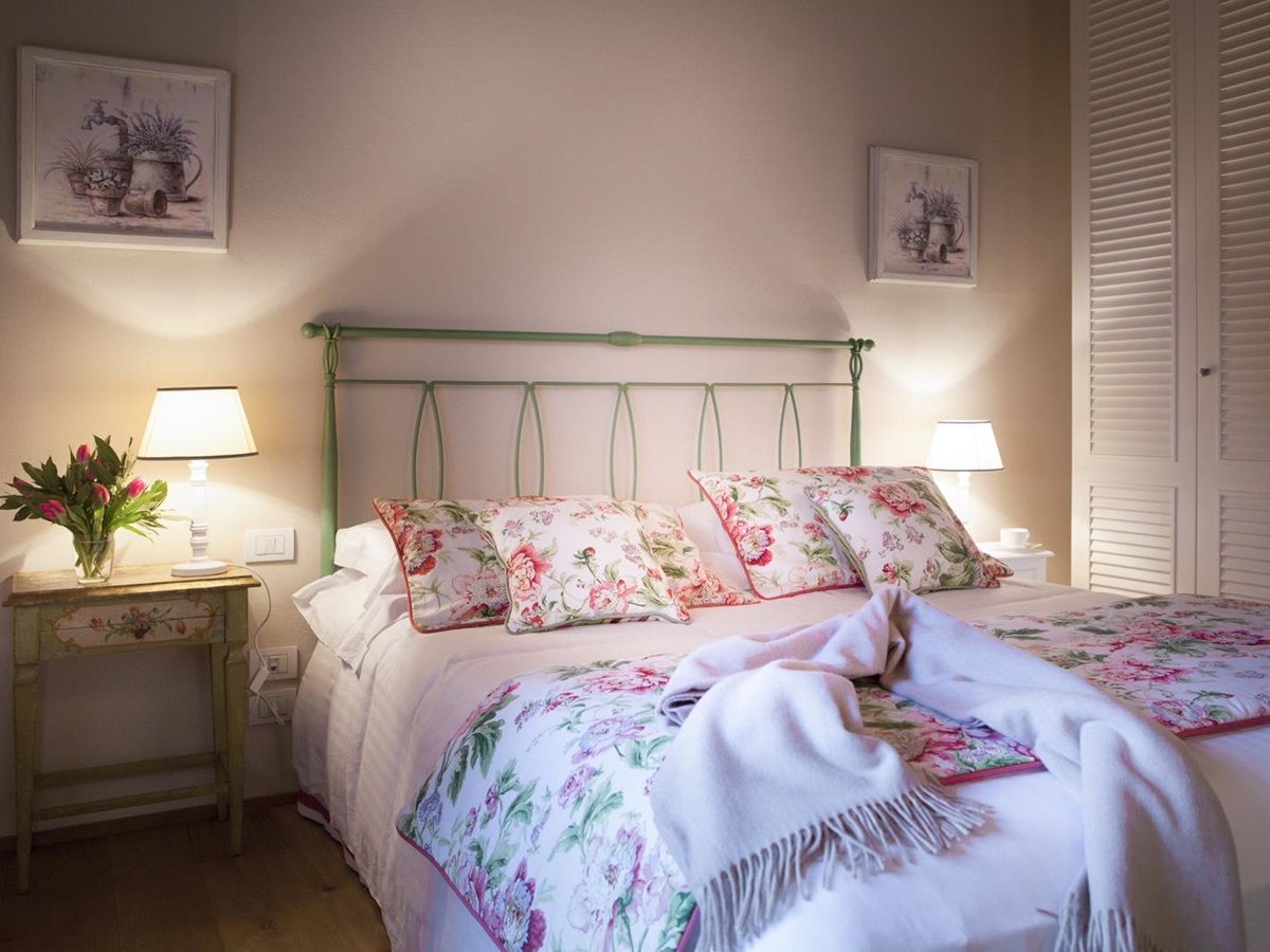Bedroom with double bed, bedside tables, lamps, flowers, wardrobe and pictures at Villa di Tignano in Tuscany, Italy