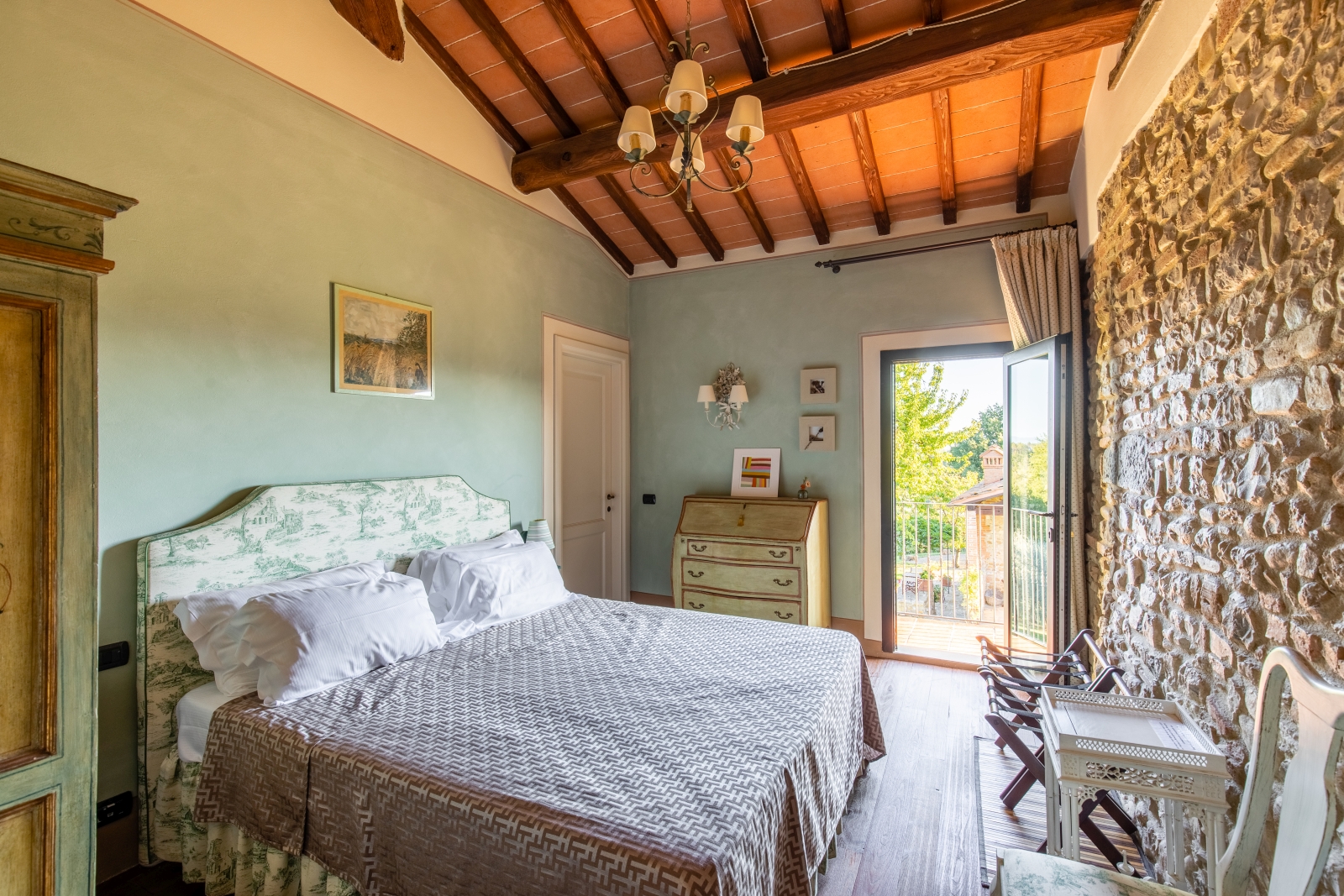 Bedroom with double bed, chairs, table, chest of drawers, painting and door to balcony at Villa Giuliana in Tuscany, Italy