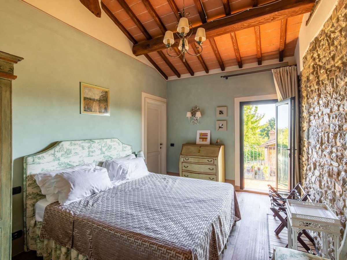 Bedroom with double bed, chairs, table, chest of drawers, painting and door to balcony at Villa Giuliana in Tuscany, Italy