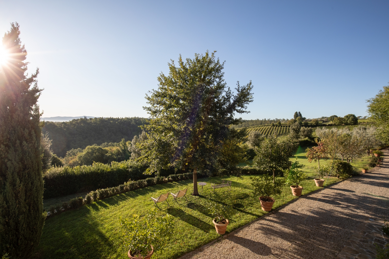 Garden with plants, benches and countryside view next to stone driveway at Villa Giuliana in Tuscany, Italy