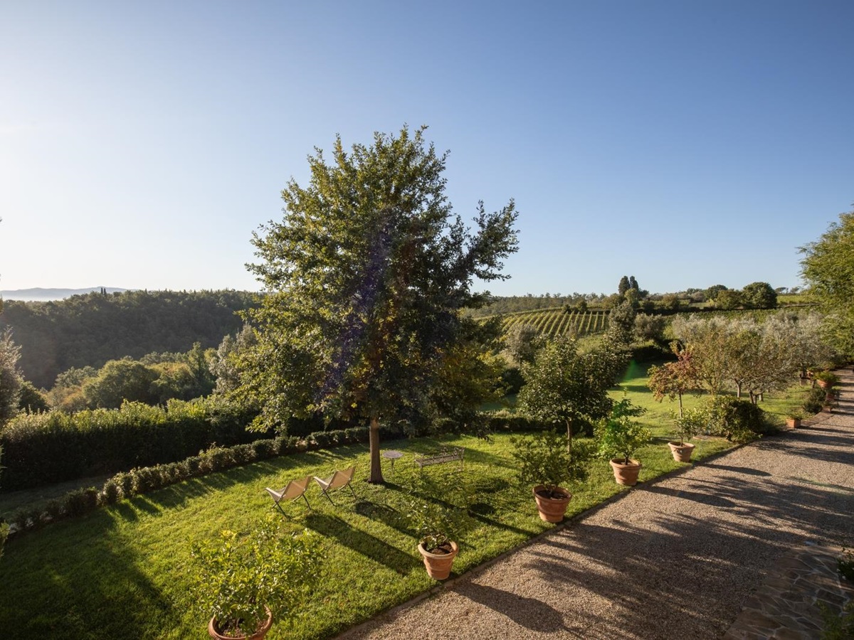 Garden with plants, benches and countryside view next to stone driveway at Villa Giuliana in Tuscany, Italy