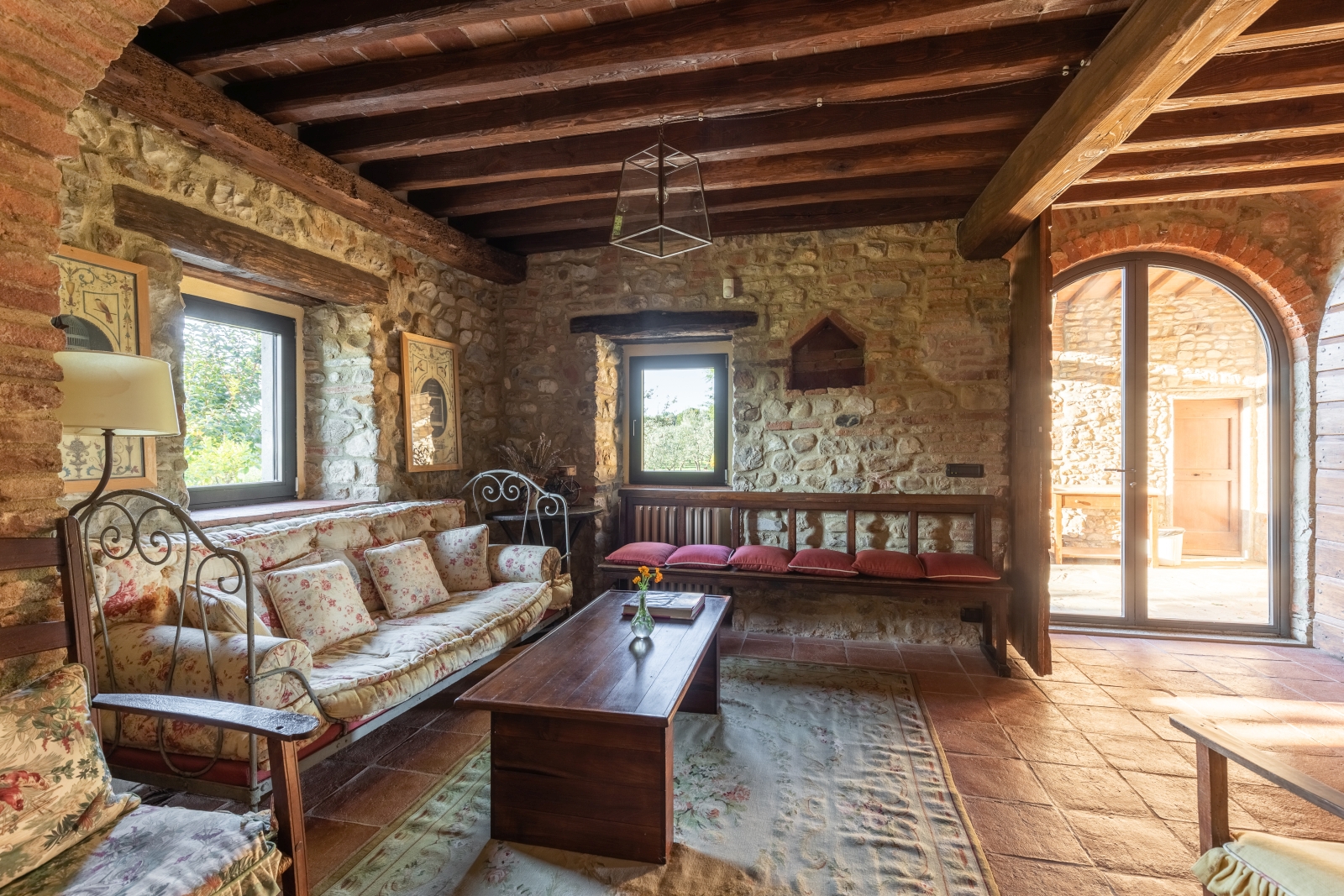 Lounge area with sofas, bench, coffee table, stone walls and French doors to garden at Villa Giuliana in Tuscany, Italy