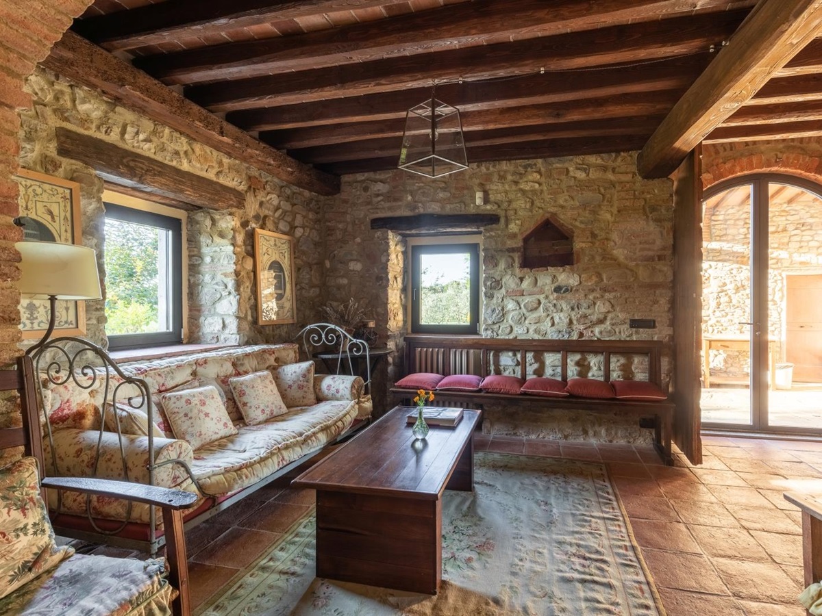 Lounge area with sofas, bench, coffee table, stone walls and French doors to garden at Villa Giuliana in Tuscany, Italy