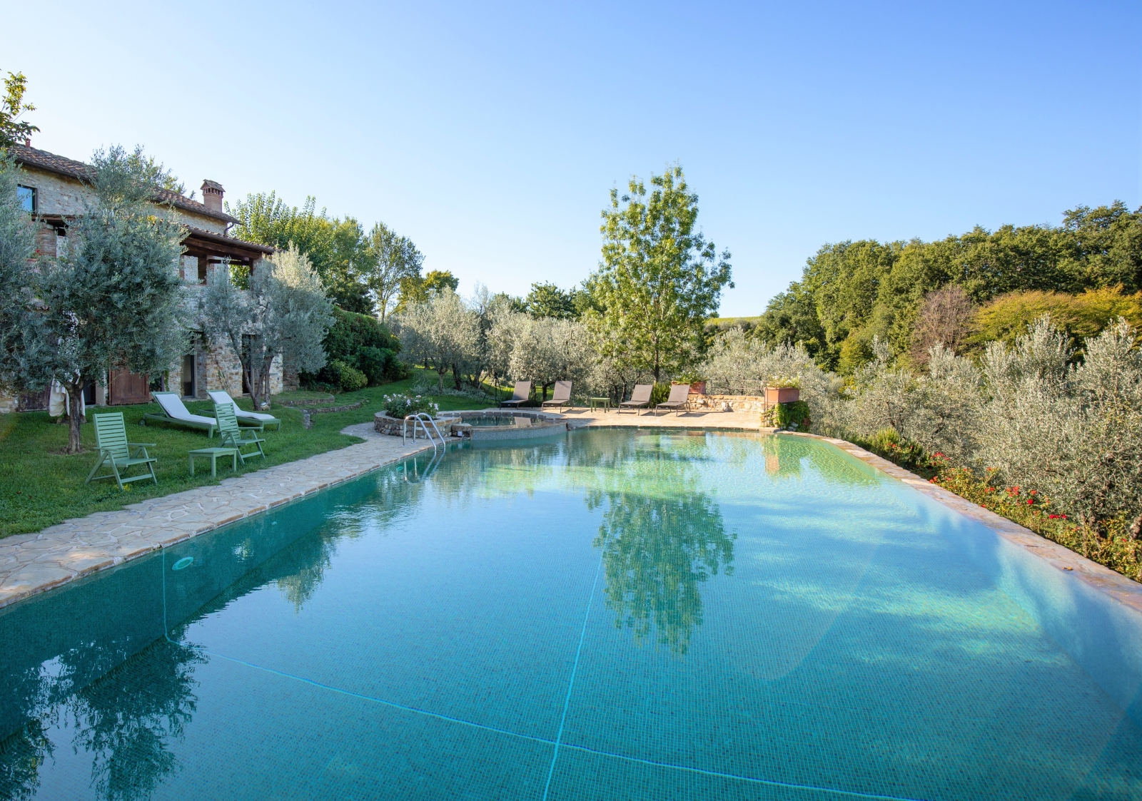 Pool at back of house with patio area, sun loungers, trees and umbrella at Villa Giuliana in Tuscany, Italy
