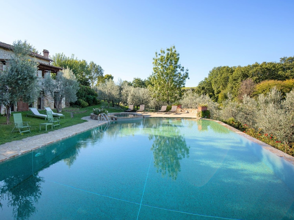 Pool at back of house with patio area, sun loungers, trees and umbrella at Villa Giuliana in Tuscany, Italy