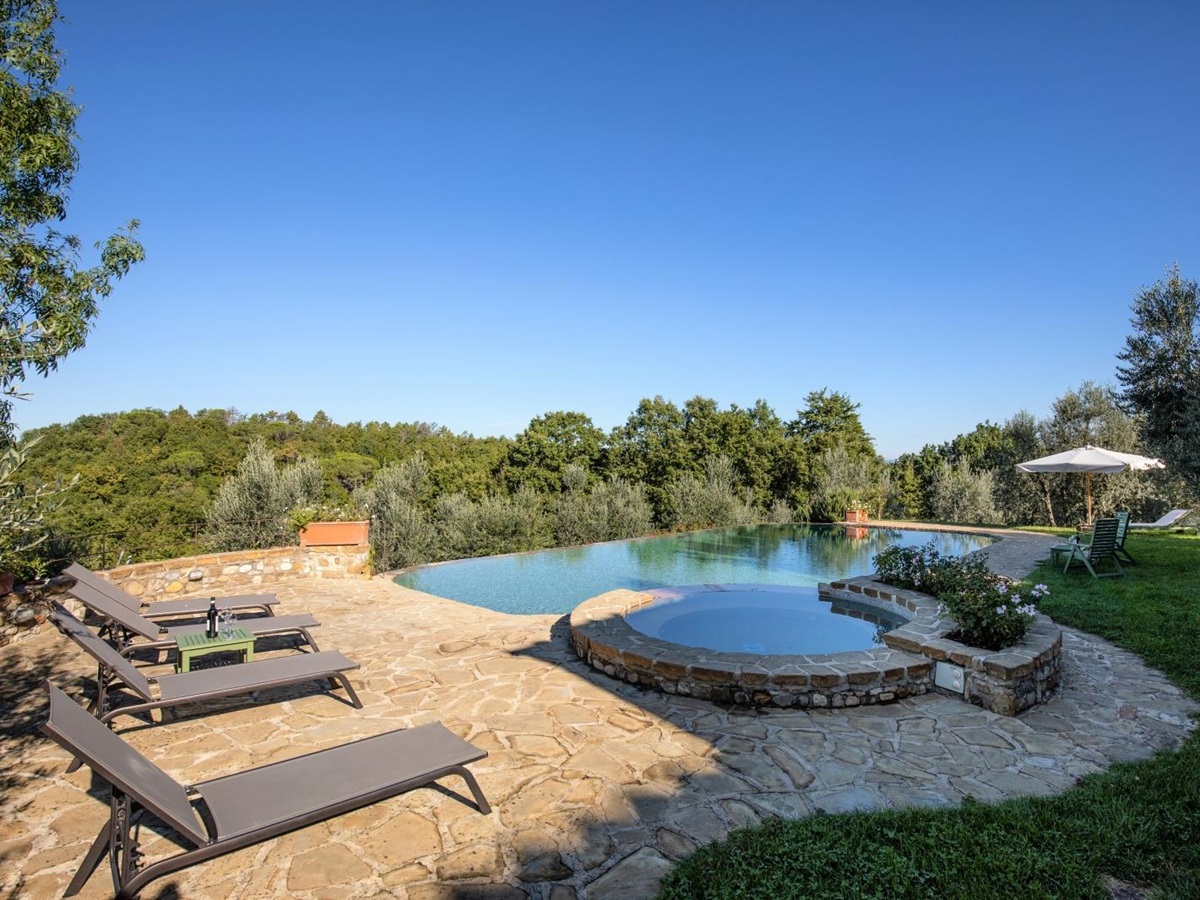 Patio next to pool with sun loungers, table, wine, umbrella and countryside view at Villa Giuliana in Tuscany, Italy