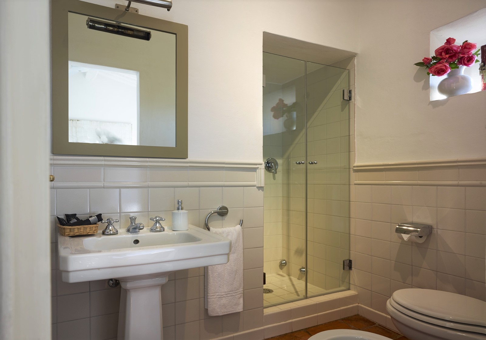 Bathroom with sink, mirror, shower, flowers and toilet at Villa La Castellana in Tuscany, Italy