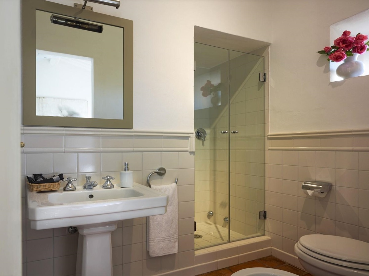 Bathroom with sink, mirror, shower, flowers and toilet at Villa La Castellana in Tuscany, Italy