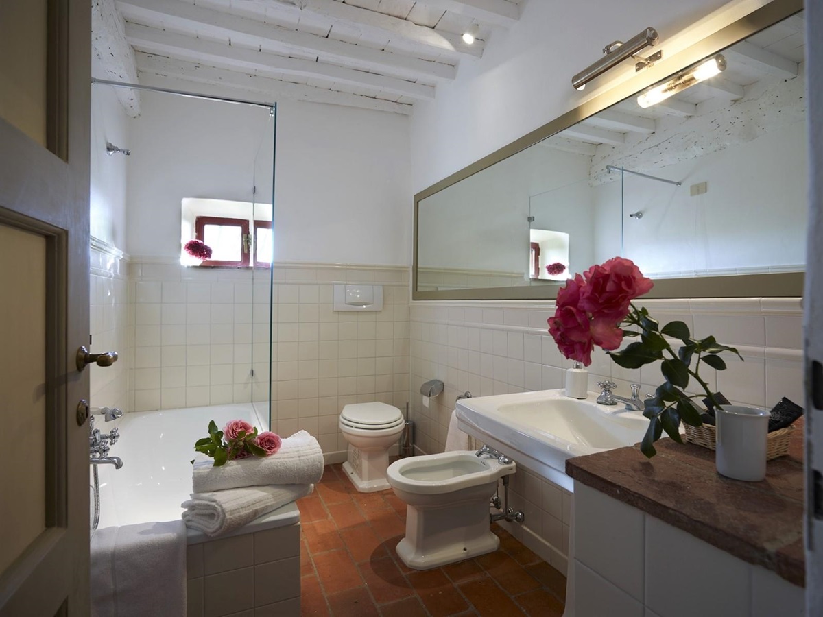 Bathroom with bath shower, toilet, bidet, long mirror, sink and flowers at Villa La Castellana in Tuscany, Italy