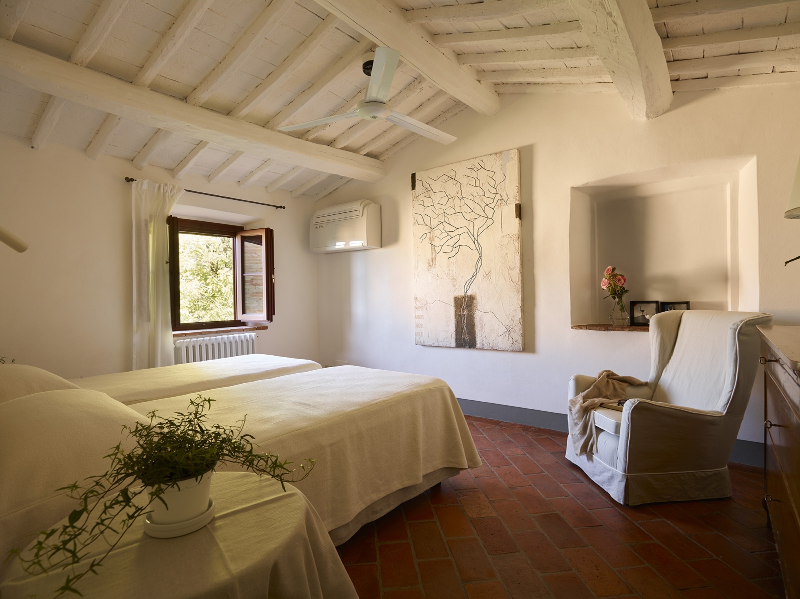 Twin bedroom with flowers, painting, bedside table and plant and armchair at Villa La Castellana in Tuscany, Italy