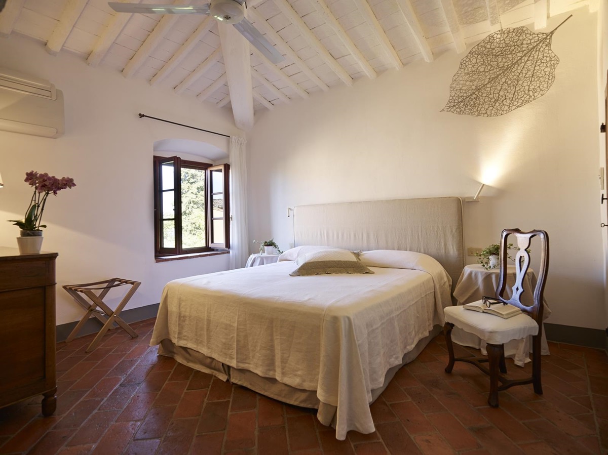 Bedroom with double bed, bedside tables, plants, flowers, chair and window at Villa La Castellana in Tuscany, Italy