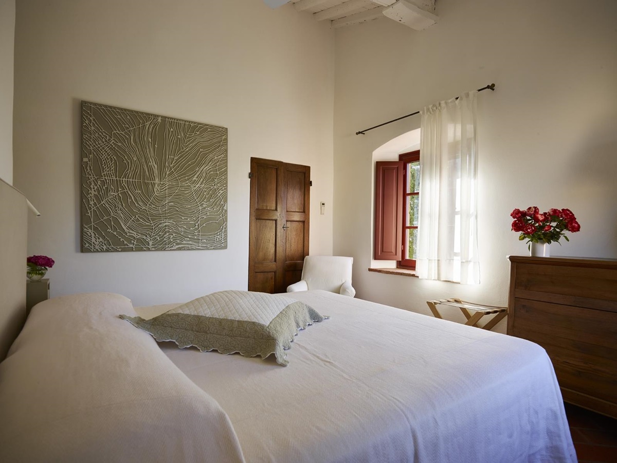 Bedroom with double bed, artwork, flowers and armchair at Villa La Castellana in Tuscany, Italy