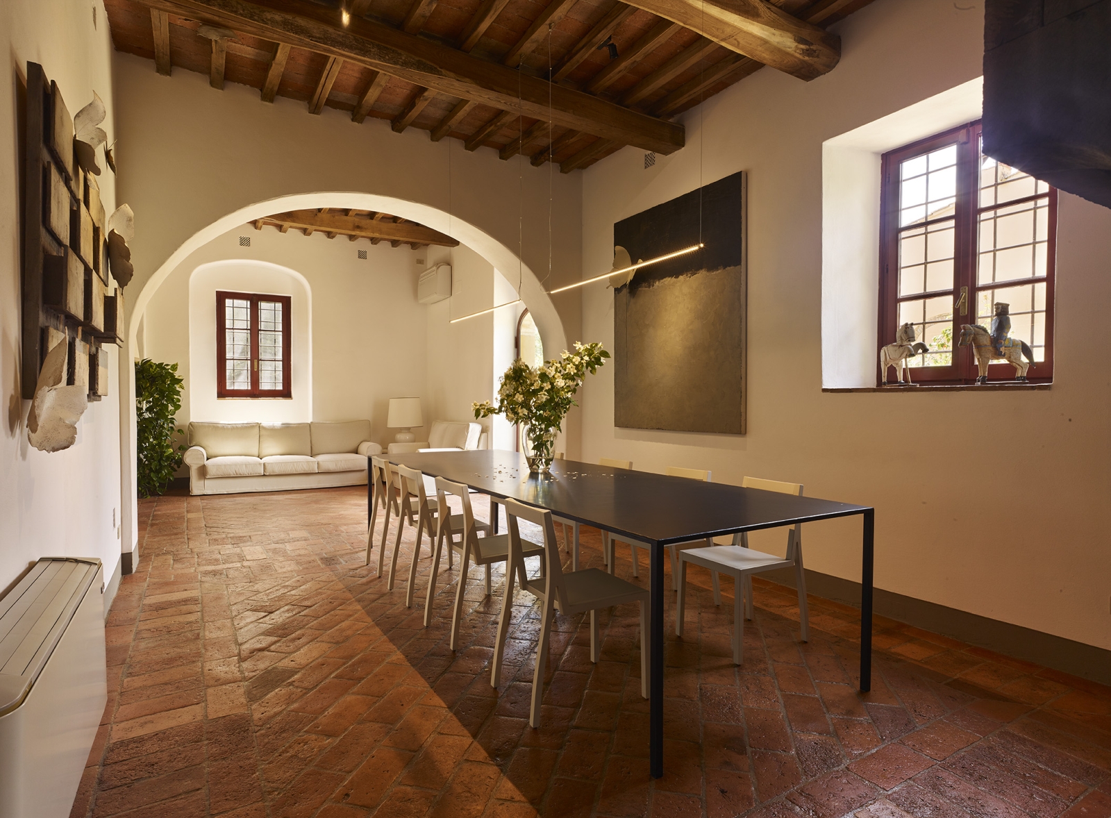 Dining room with long dining table, artwork, horse statues and sofas at Villa La Castellana in Tuscany, Italy