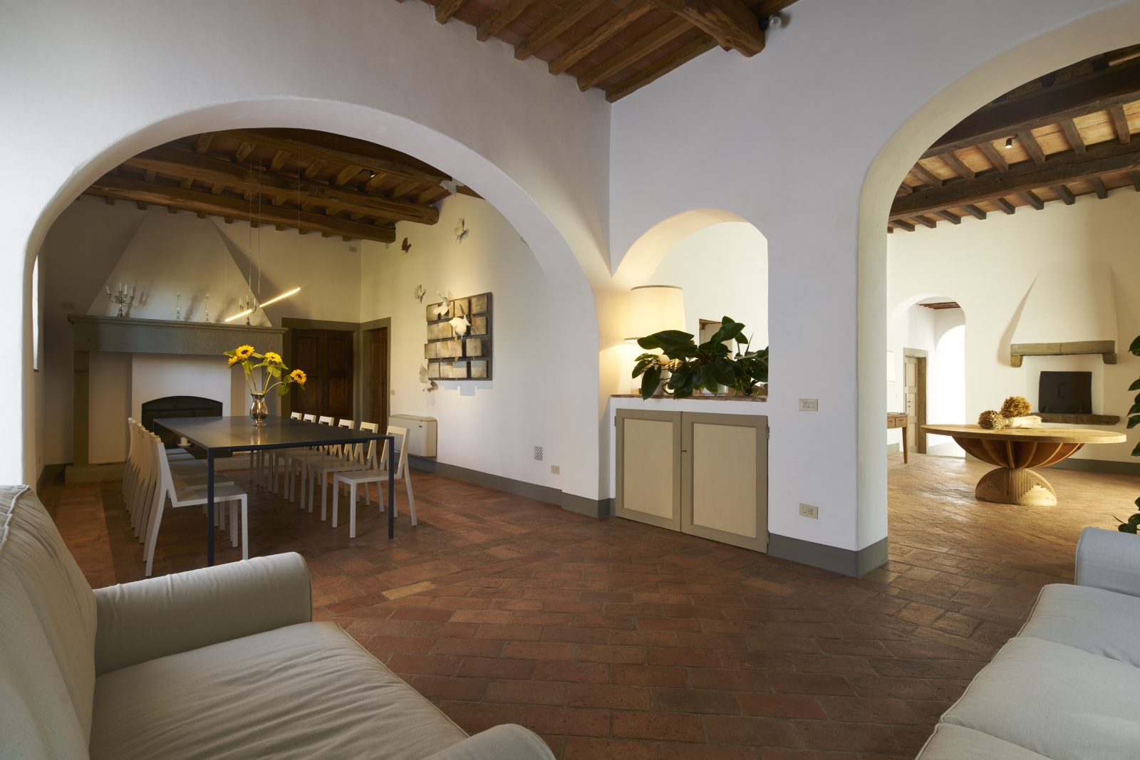 Dining area with long dining table, fireplace, sofas and archway to entrance hall at Villa La Castellana in Tuscany, Italy