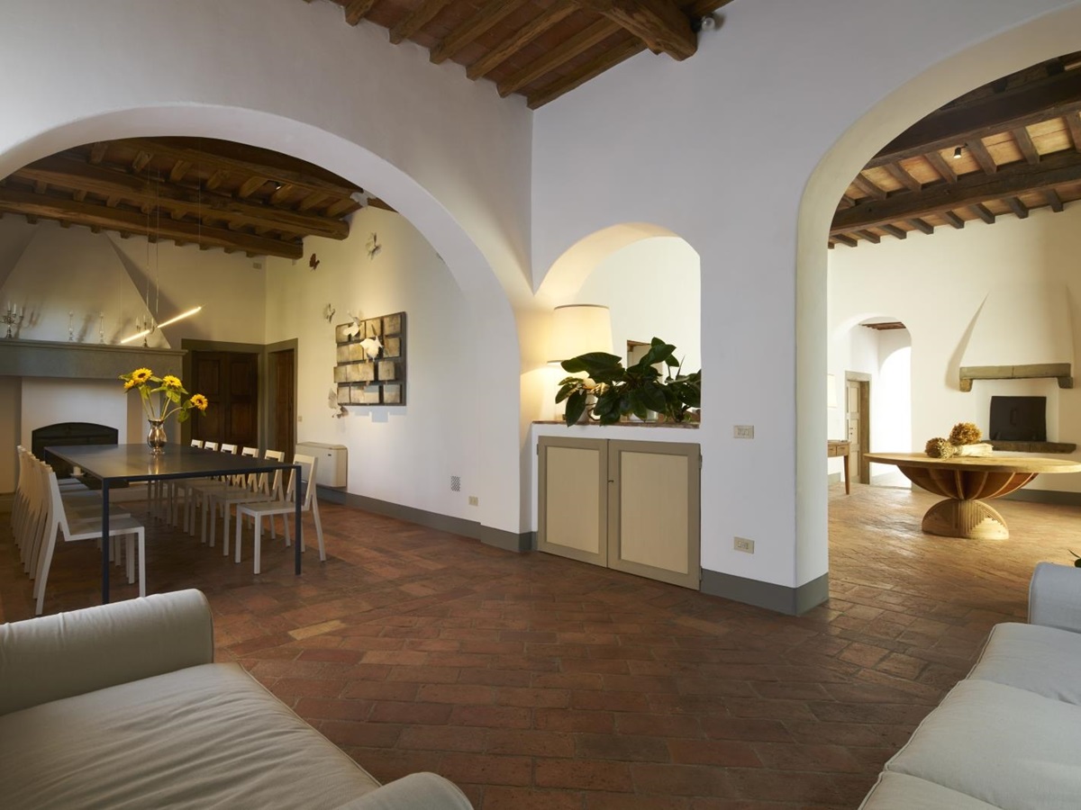 Dining area with long dining table, fireplace, sofas and archway to entrance hall at Villa La Castellana in Tuscany, Italy