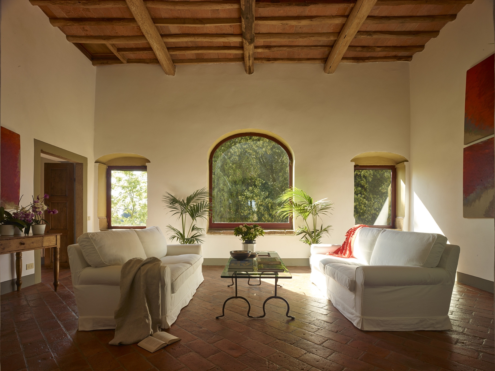 Living room with sofas, plants, coffee table, flowers, paintings and large windows at Villa La Castellana in Tuscany, Italy