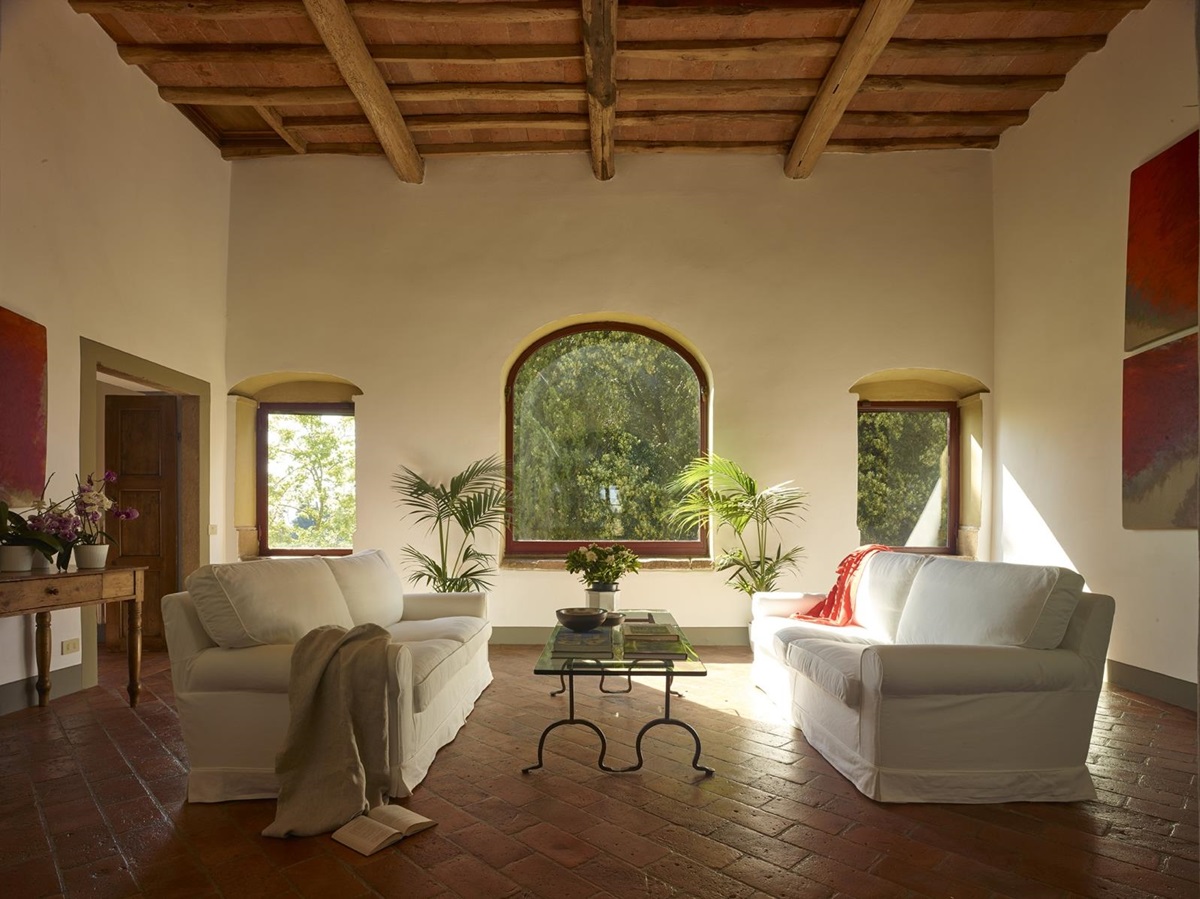 Living room with sofas, plants, coffee table, flowers, paintings and large windows at Villa La Castellana in Tuscany, Italy