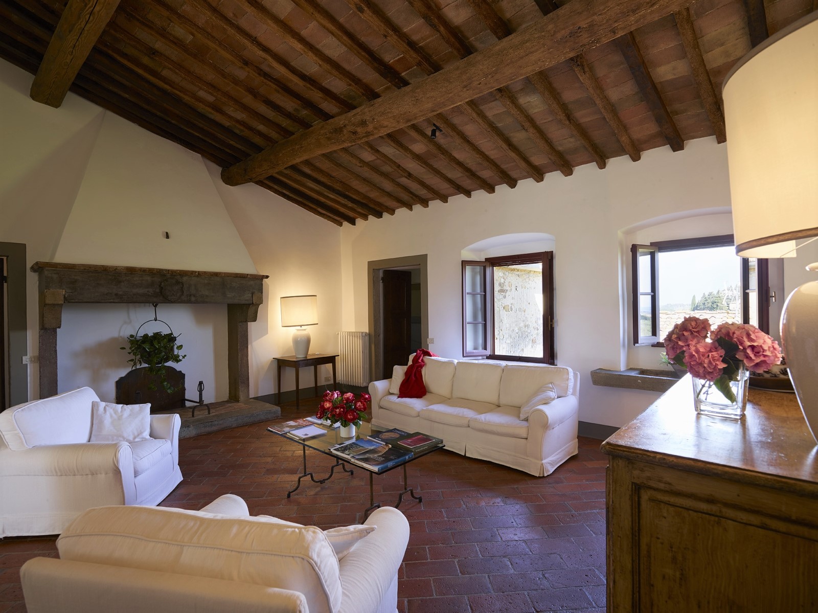Sitting room with armchairs, sofa, coffee table, flowers lamps and fireplace at Villa La Castellana in Tuscany, Italy