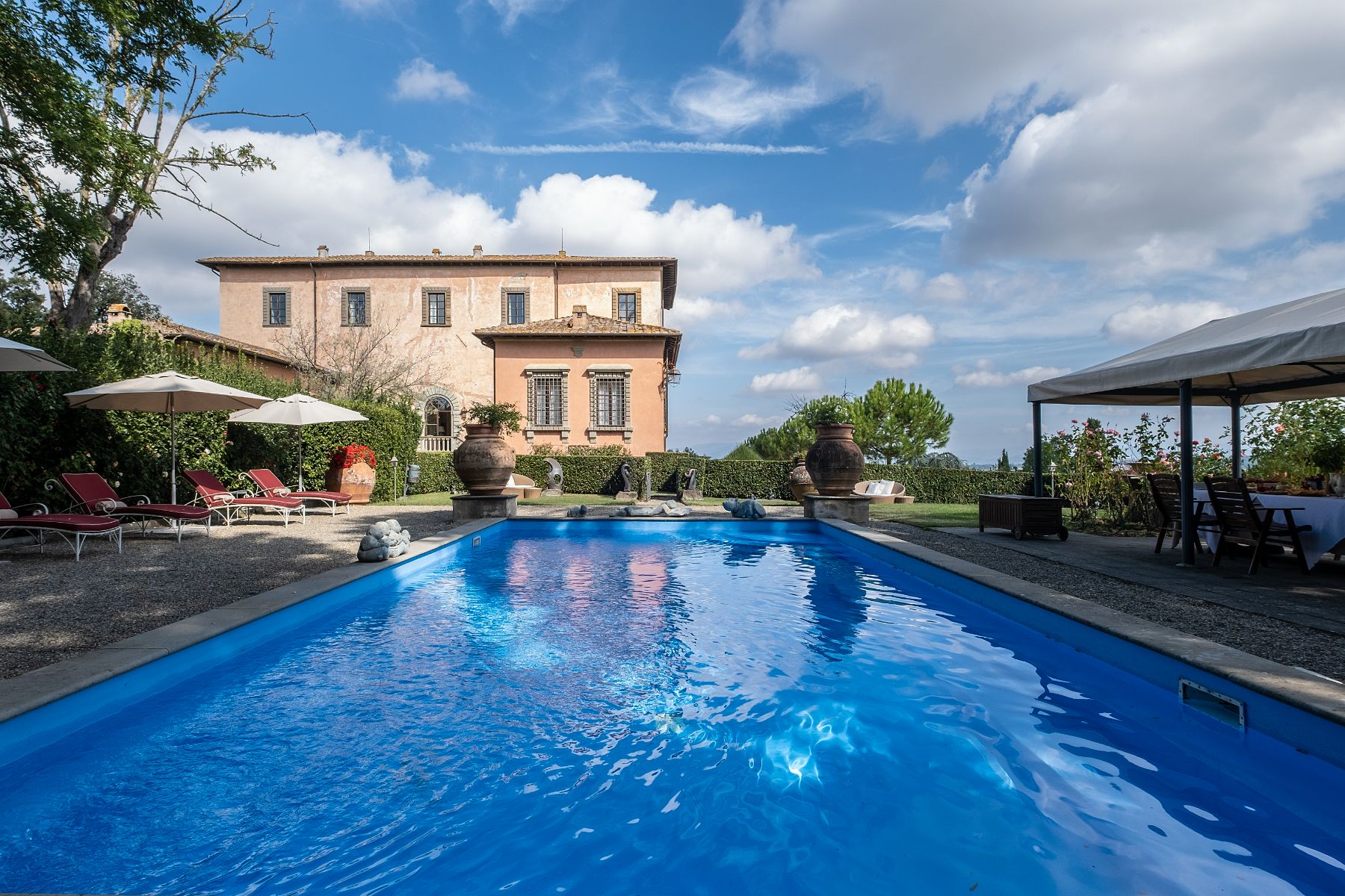 Outdoor pool with red sun loungers and view of Villa Machiavelli