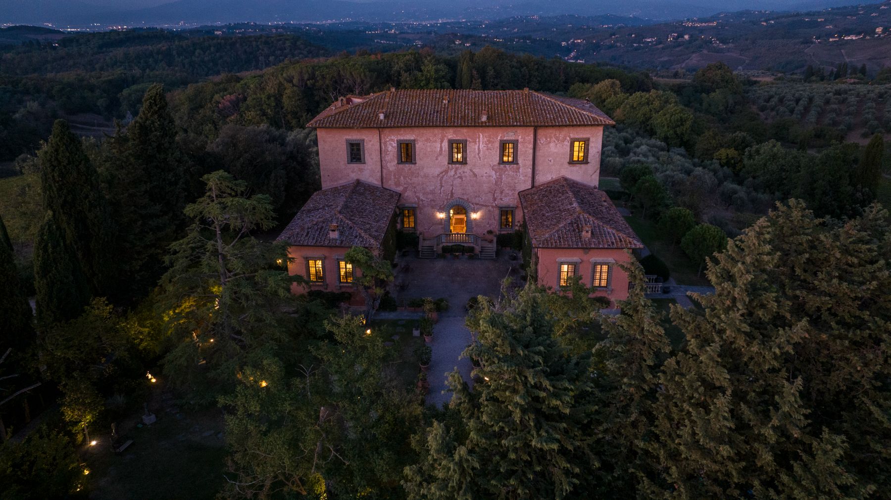 View of Villa Machiavelli in Tuscany at night surrounded by rolling hills and lights from nearby towns in the distance