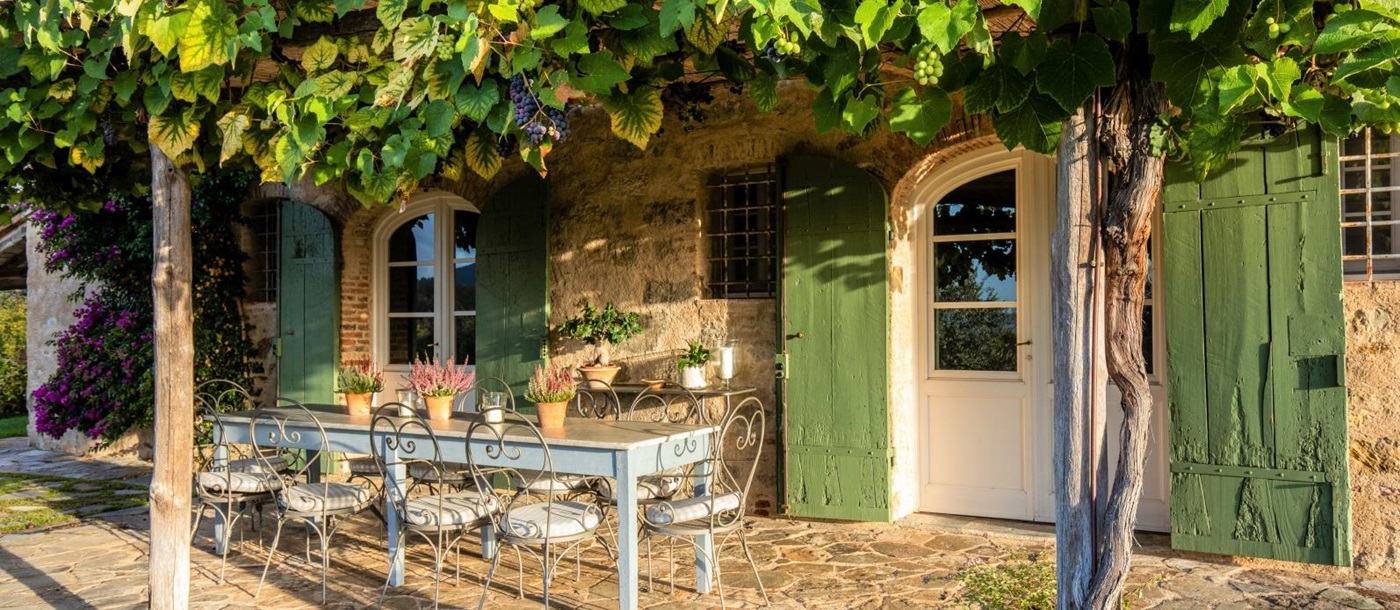 Outdoor dining area with long table, chairs, flowers and vines with grapes at Villa Ortensia in Tuscany, Italy