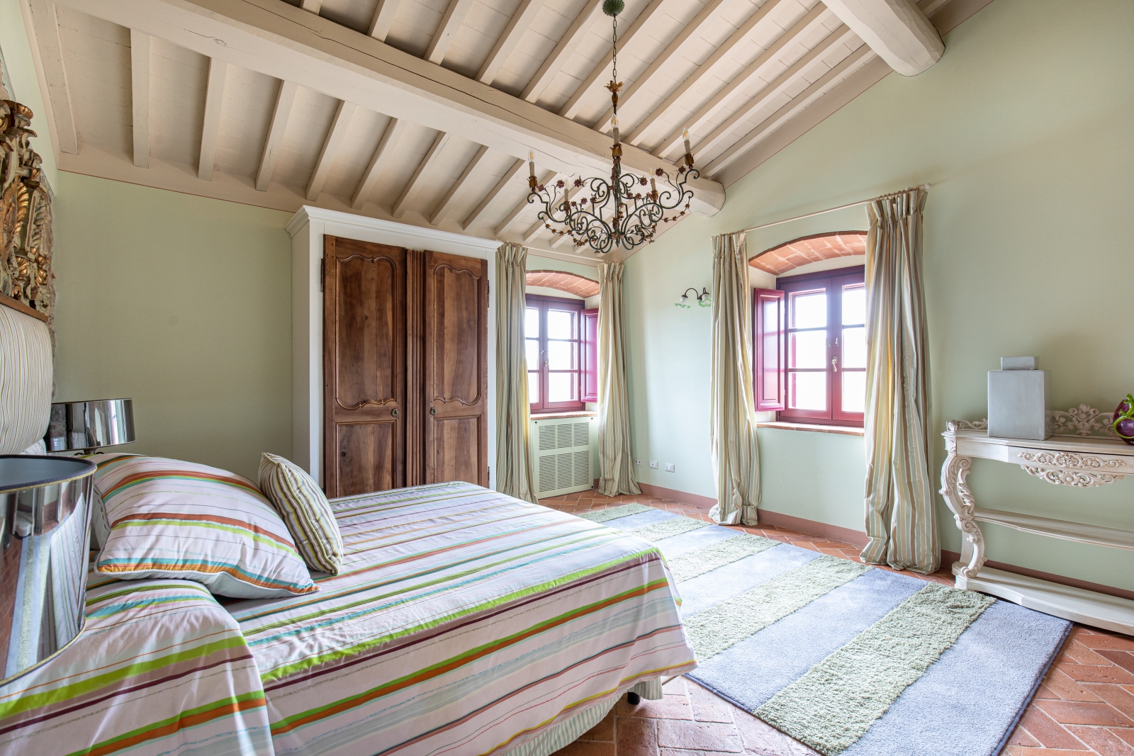 Bedroom with double bed, wardrobe, chandelier, windows, rug, table and green walls at Villa Papavero in Tuscany, Italy