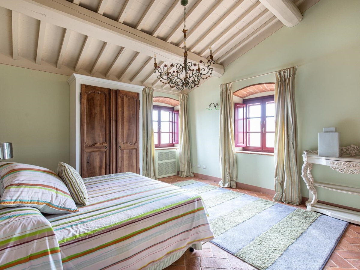 Bedroom with double bed, wardrobe, chandelier, windows, rug, table and green walls at Villa Papavero in Tuscany, Italy