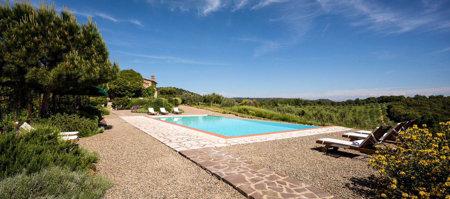 Pool with patio area, sun loungers, plants, trees, flowers and countryside view at Villa San Barberino in Tuscany, Italy