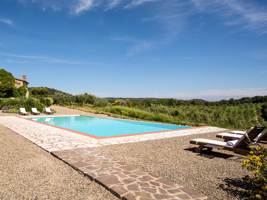 Pool with patio area, sun loungers, plants, trees, flowers and countryside view at Villa San Barberino in Tuscany, Italy