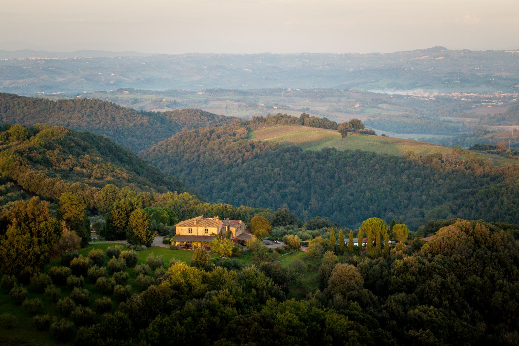 Drone view of Villa San Barberino surrounded by hills and trees in Tuscany