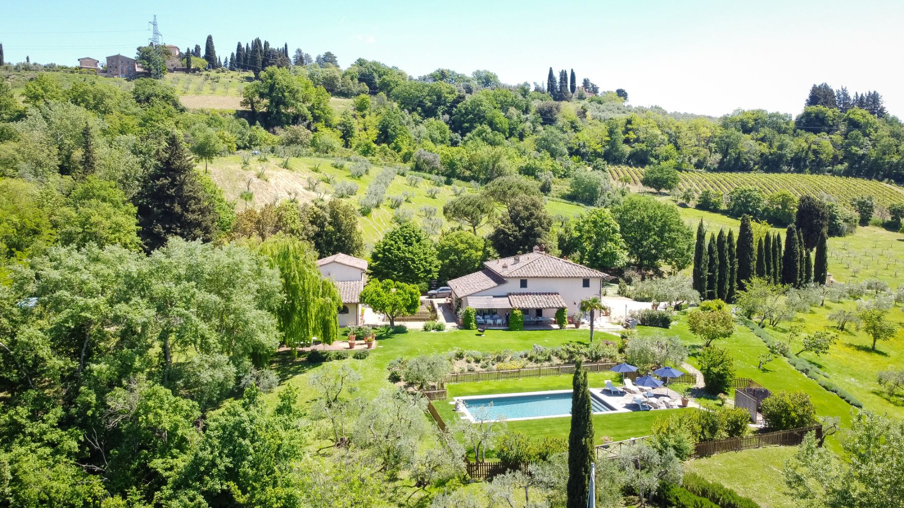 Drone view of Villa San Cascinano in Tuscany surrounded by Tuscan hills and trees with view of the outdoor pool